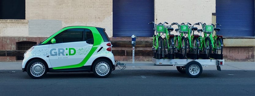 Small GR:D electric vehicle pulling a trailer loaded with GR:D bicycles.