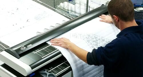 A man feeding a large document into document scanning equipment at a commercial printers.