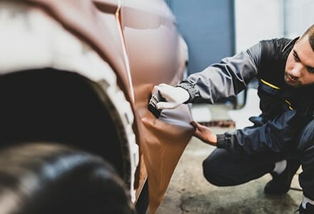 print installer applying color change vinyl to a vehicle with a squeegee careers in commercial printing