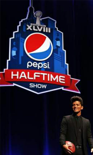 Photo of Bruno Mars holding a basketball with a large printed sign for the Pepsi halftime show.