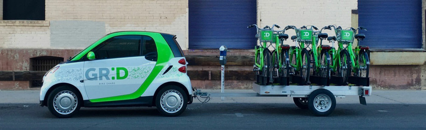 Profile shot of a smart car wrap hauling a trailer for of green bikes.