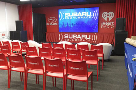 Subaru trade show booth with 3 rows of red chairs displaying the Subaru logo.