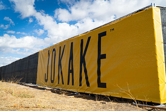JOKAKE logo on large yellow mesh fence banner