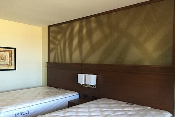 Hotel room bed headboard wrapped with vinyl graphics in the design of palm leaves.