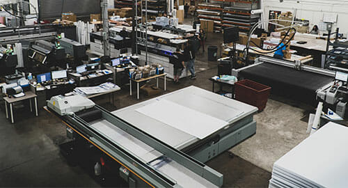 Production floor of a commercial printing company featuring a flatbed printer in the foreground.