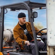 man with a black beanie and brown jacket driving a forklift.