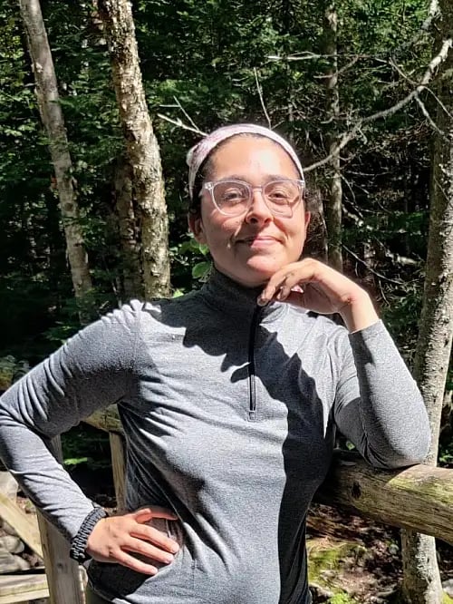Person posing outdoors near trees.