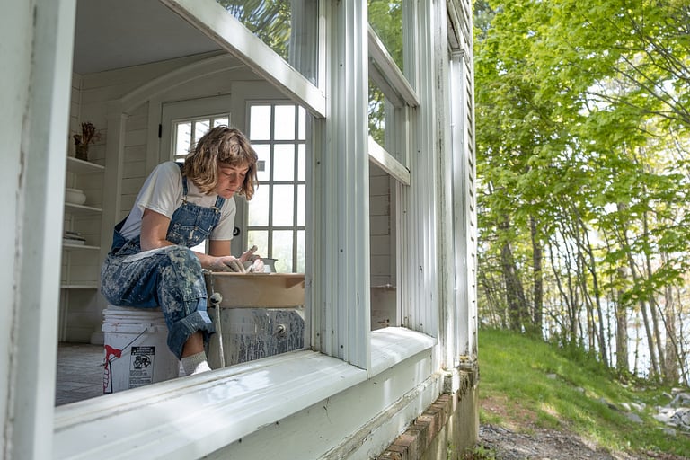 Person sculpting pottery by window