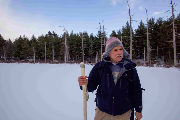 Steve outside with winter hat and walking stick on a frozen lake