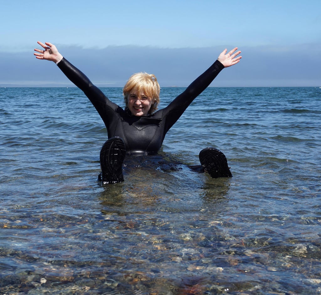 piper in a wetsuit sitting in shallow ocean water