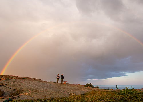 Two people under a rainbow sky.