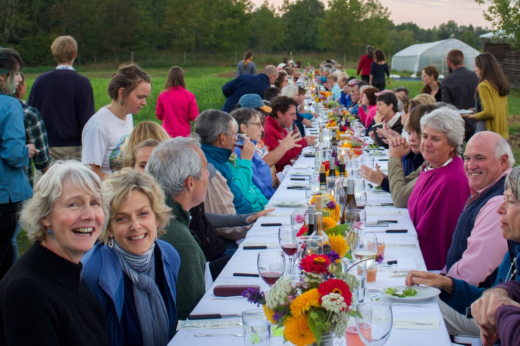 many people at a long table eating dinner outside at dusk