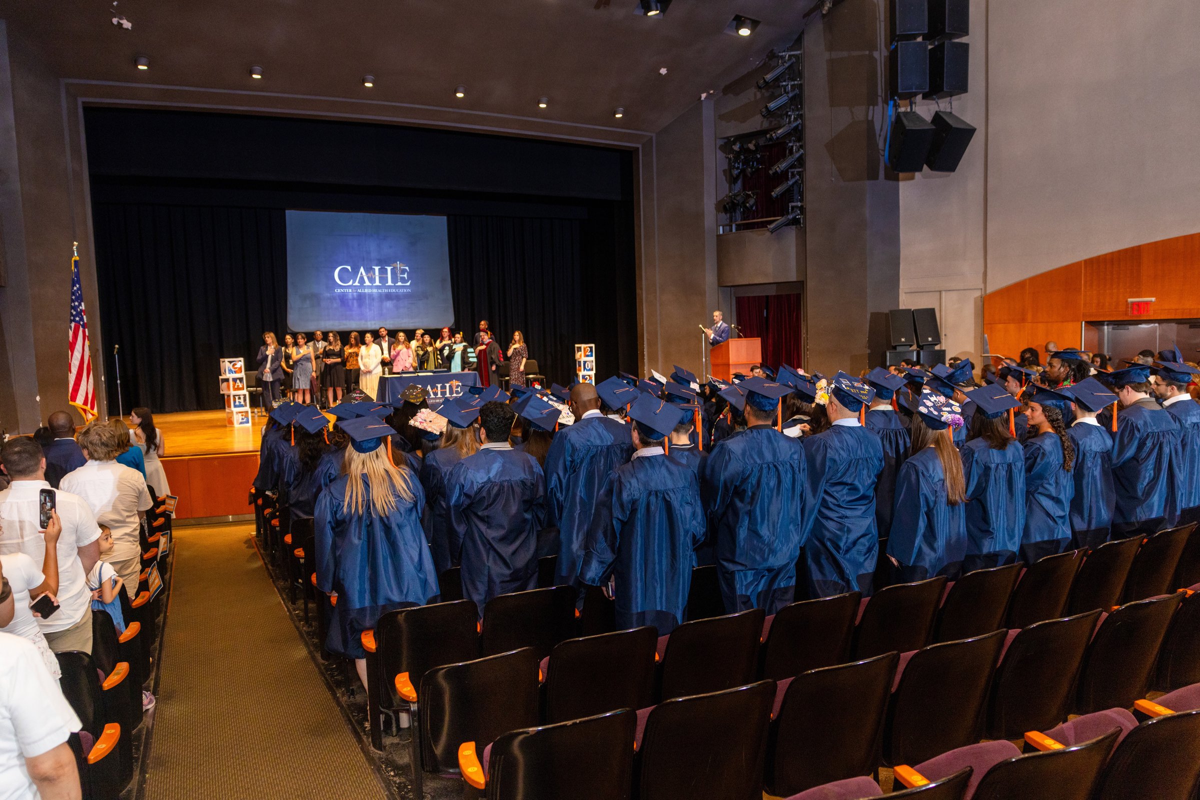 CAHE graduates seated in an auditorium facing the stage