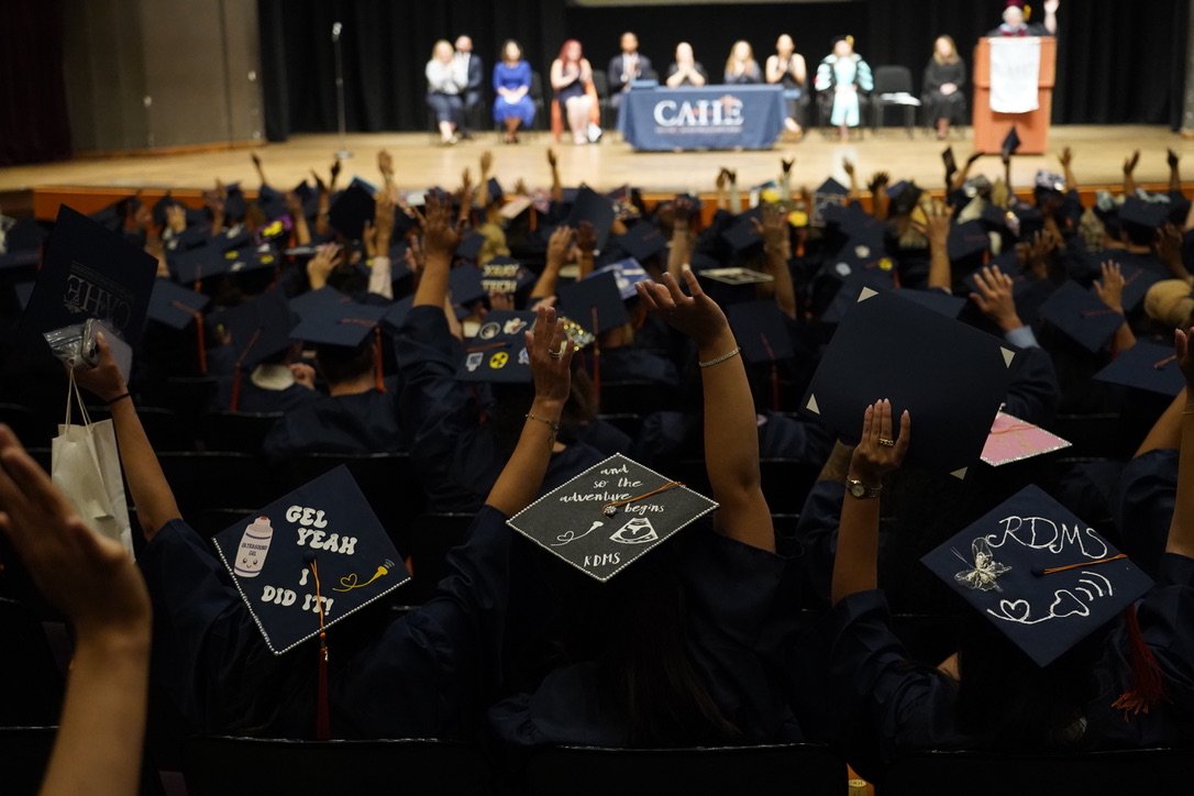 Close-up of decorated CAHE graduation mortarboard caps with orange tassels.