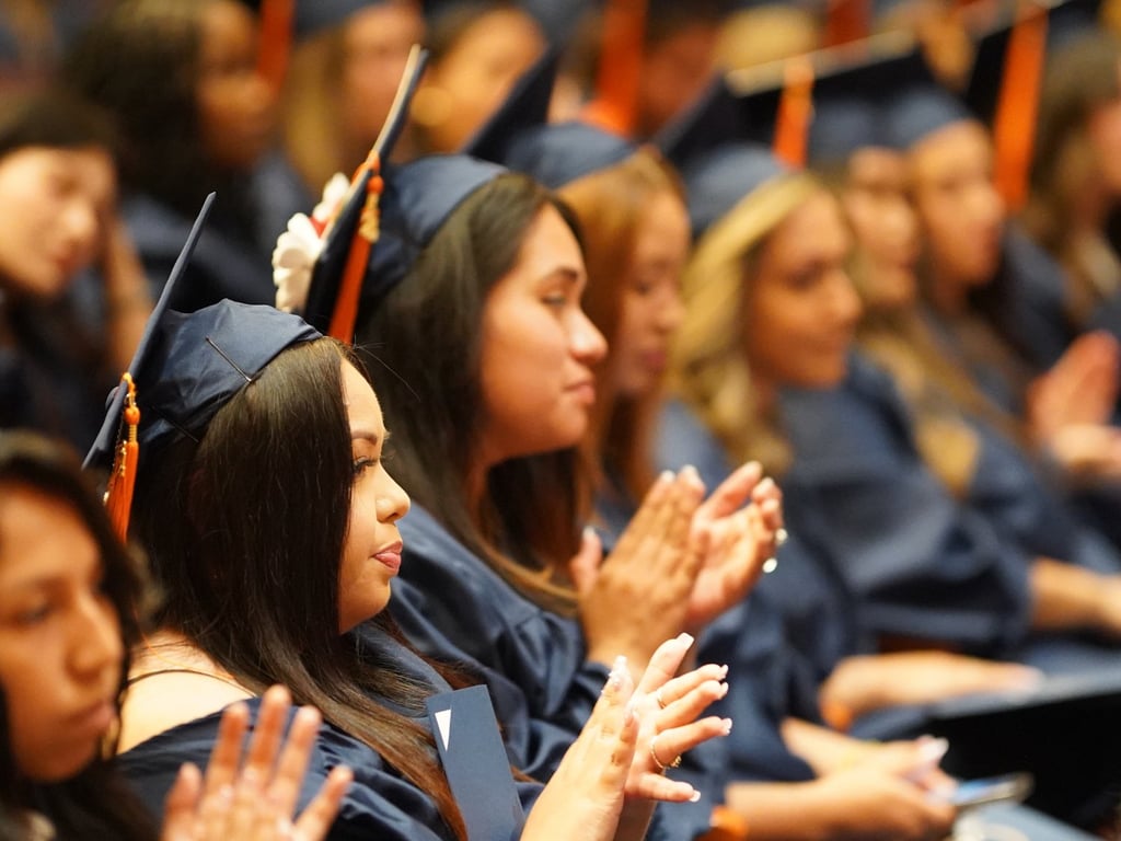 CAHE graduates in navy blue caps and gowns celebrating at a commencement ceremony.