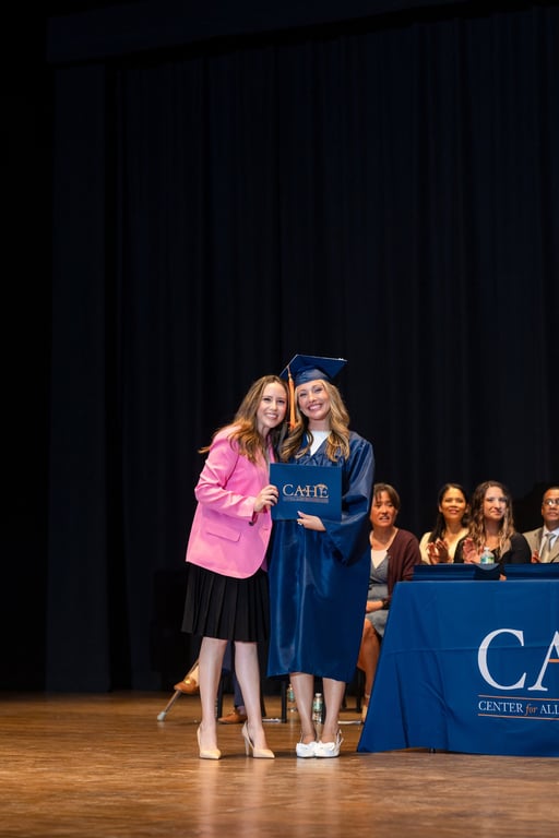 A CAHE faculty member and graduate pose together at commencement in academic attire.