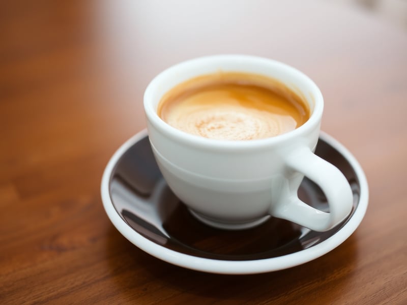 a close-up of a double espresso in a white ceramic cup on a dark timber saucer, rich crema on top, soft natural side light, shallow depth of field, minimalist cafe setting