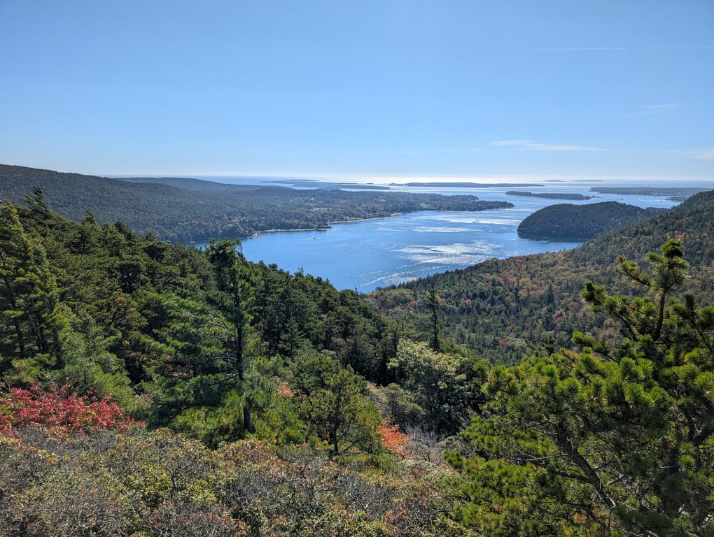 Image with caption 'This was the first mountain-top view on this trip. It set a pretty good baseline. Our goal for the trip was to see some fall foliage, which you can see a little bit of in small patches (there are a lot of pine trees and other evergreens in Acadia).'