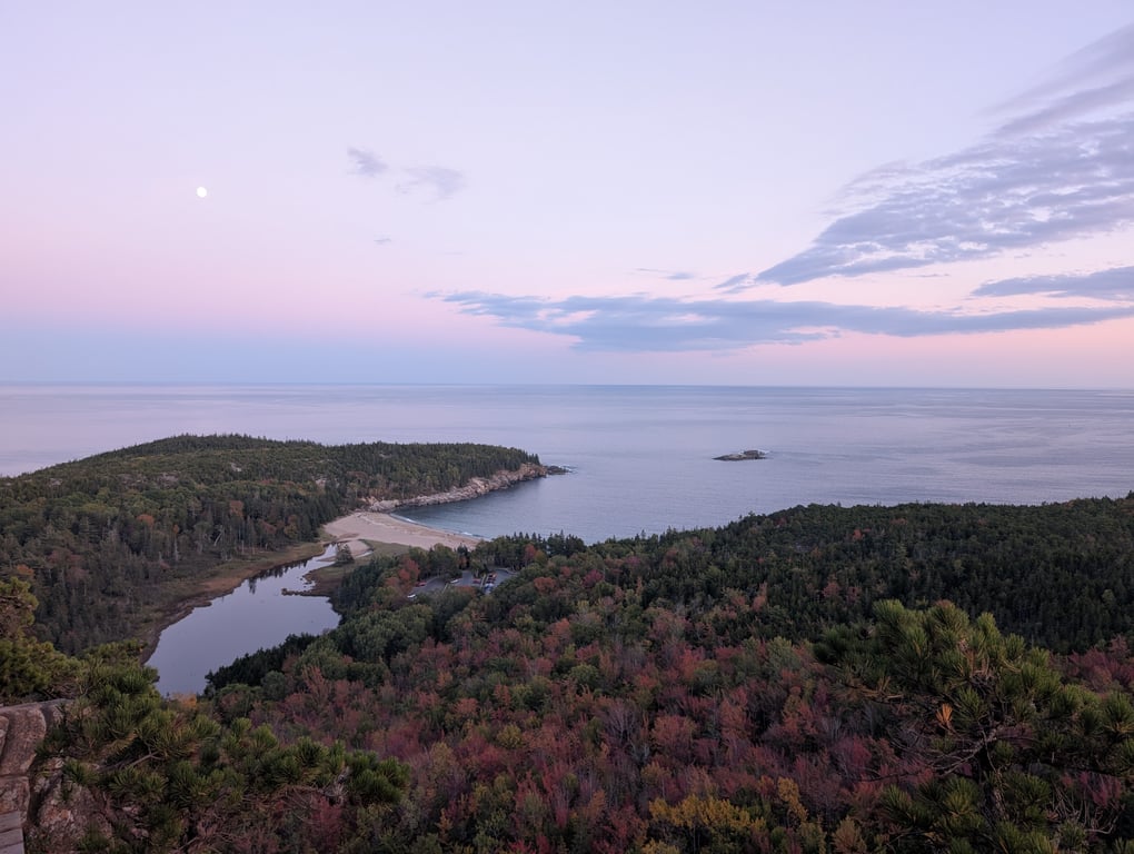 Image with caption 'Using the last vestiges of daylight, we had great views down towards the water. That beach is where we'd later all reconvene. The fall foliage on this face of this mountain is the brightest that we saw this entire trip (although the photo doesn't do the colors justice).'