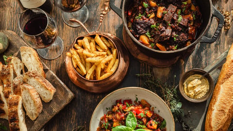 Mesa de cena francesa rústica con Boeuf Bourguignon, Steak Frites crujientes y una botella de vino tinto.