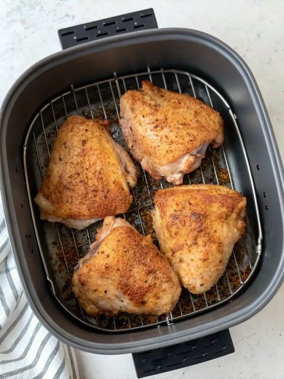 Fully cooked air fryer chicken thighs plated with fresh herbs and lemon wedges