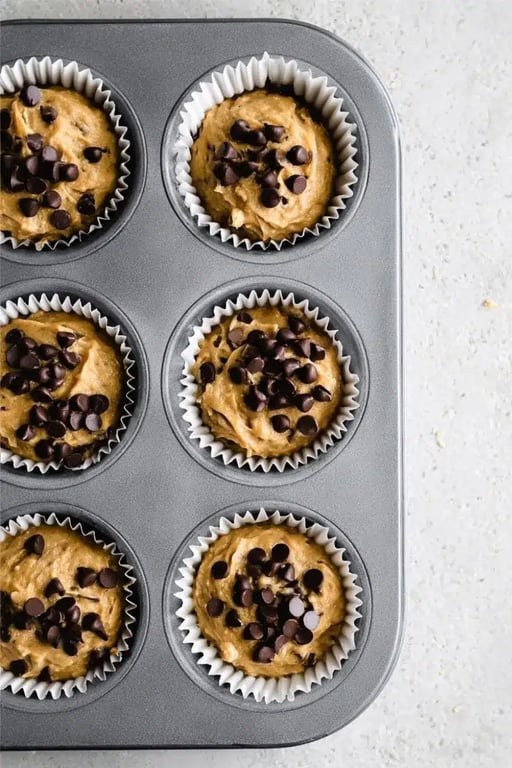 Banana protein muffin batter in a muffin tin topped with chocolate chips.
