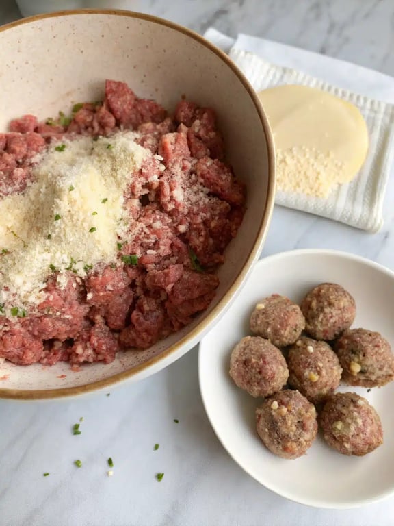Hands forming raw ground beef mixture into round meatballs for the creamy mushroom dish