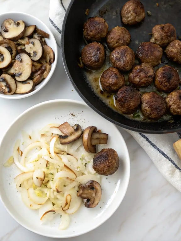 Sliced mushrooms and onions sautéing in a skillet for the creamy mushroom meatball sauce