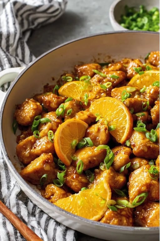 Healthy Orange Chicken Recipe That’s Better Than Takeout 1 Close-up of healthy orange chicken with orange slice garnish and green onions in a skillet