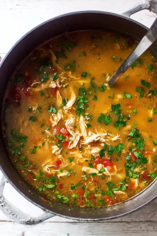 A pot of simmering keto chicken tortilla soup with shredded chicken, diced tomatoes, cilantro, and spiced broth, stirred with a ladle.