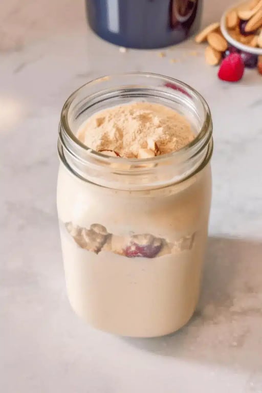 Low calorie protein shake in a glass jar, topped with almond slices and protein powder, set on a light marble surface.