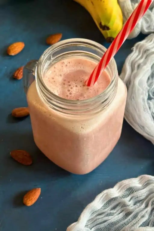 Low calorie strawberry protein shake in a glass jar with red striped straw, surrounded by almonds and a banana