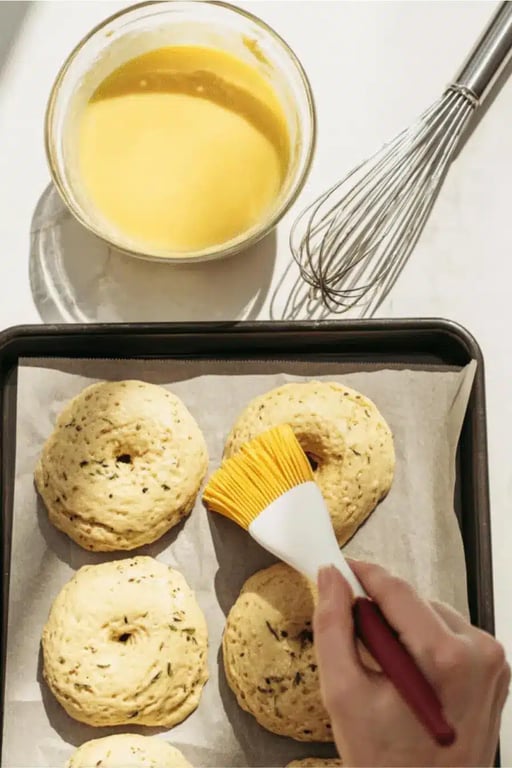 Brushing unbaked low carb bagels with smooth egg wash on a parchment-lined tray