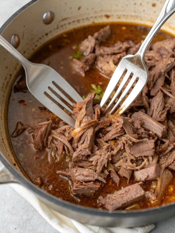 Final step for slow cooker barbacoa — shredded beef served in a warm tortilla with lime and onion