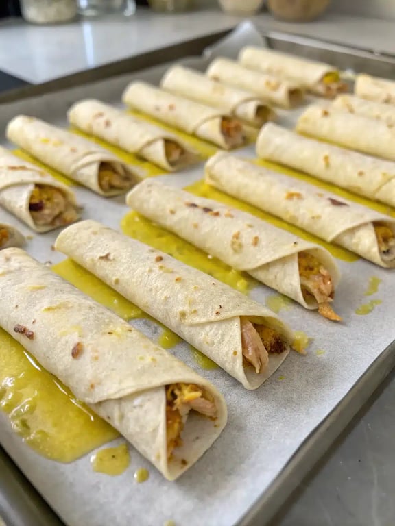A final platter of golden brown baked chicken taquitos, ready to be served with dipping sauces.