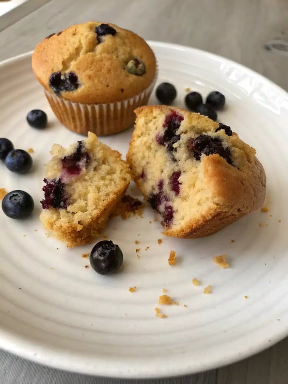 A beautifully arranged plate with a blueberry protein muffin, fresh blueberries, and a cup of coffee