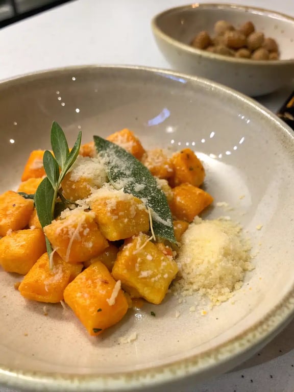 A family-style bowl of butternut squash gnocchi in brown butter sauce with salad on the side