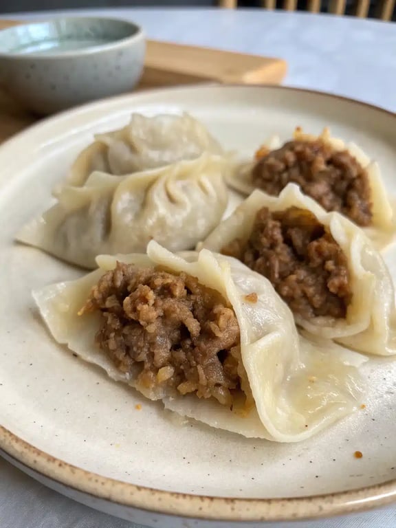 A beautifully arranged platter of ground beef dumplings with dipping sauce and garnishes.