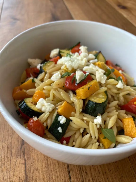 A beautifully plated bowl of roasted vegetable orzo with extra feta and parsley garnish