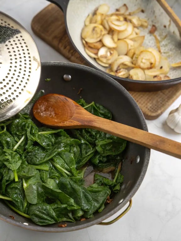 Step 2 for easy spanakopita recipe — wilting spinach in a skillet