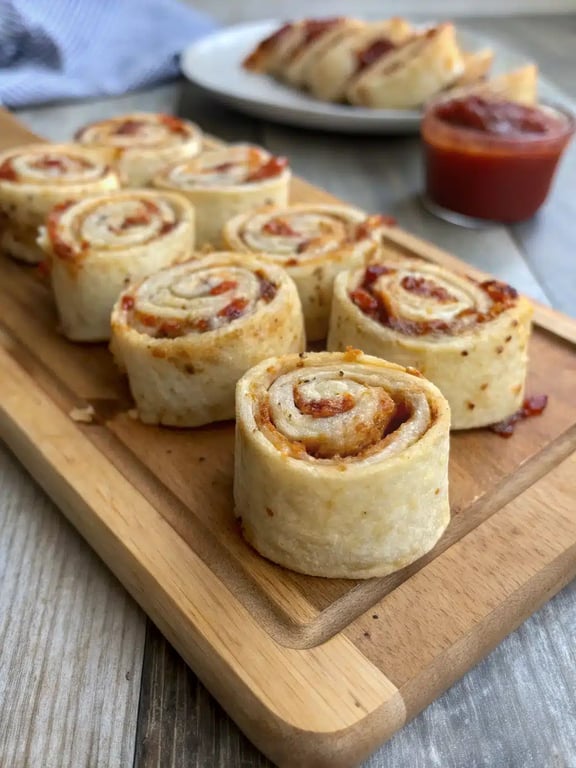 A platter of golden brown tortilla pizza rolls arranged around a bowl of dipping sauce