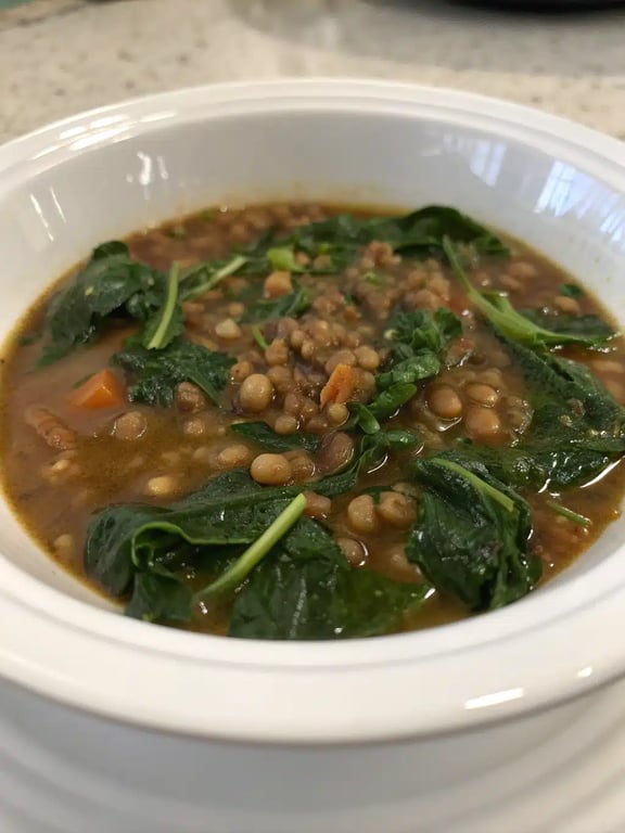 A beautifully styled bowl of spinach lentil soup with a lemon wedge and crusty bread on the side