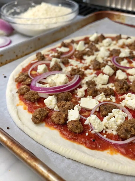 Step 4 for sausage feta pizza — assembled pizza with sausage, feta, and onion
