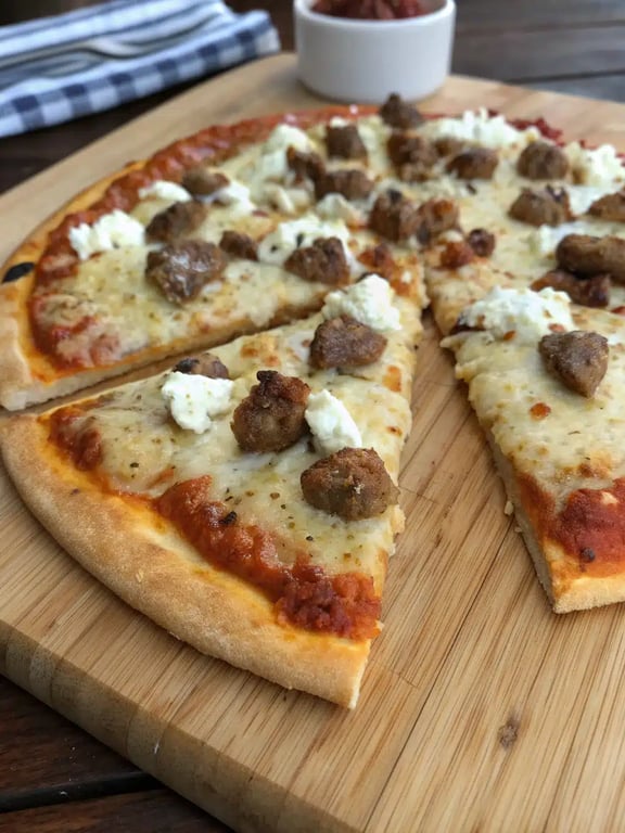 sausage feta pizza sliced and served on a wooden board with a side salad