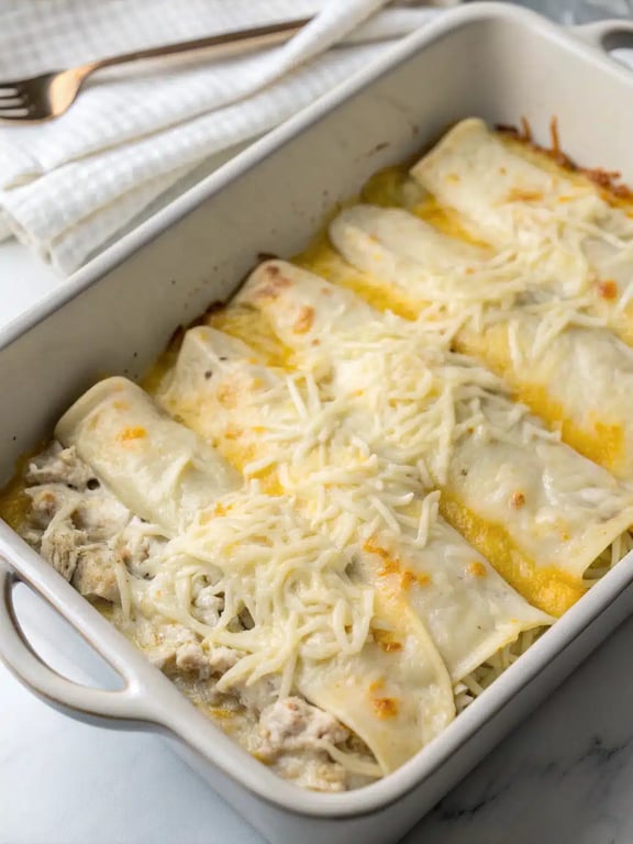 A serving of white chicken enchilada casserole on a plate with lime wedges, avocado, and a side salad