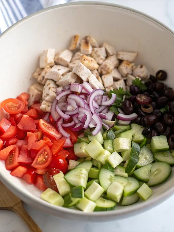 Adding warm, diced grilled chicken to the bowl of fresh vegetables