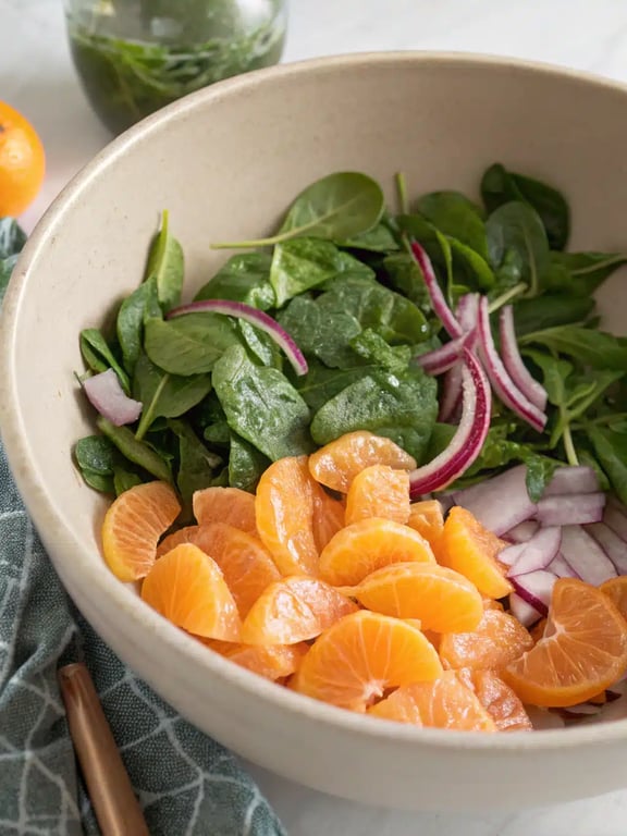 Step 4 for spinach mandarin salad — dressing being drizzled over the greens