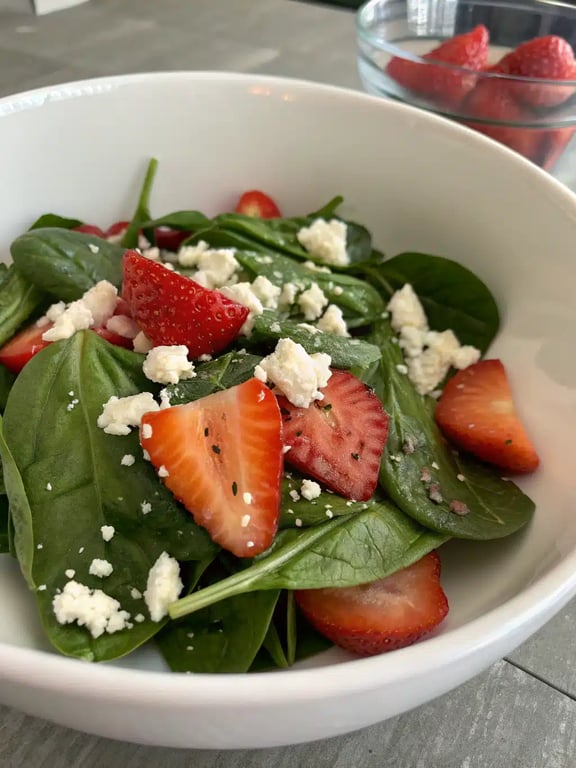 A beautifully plated strawberry spinach salad served alongside grilled chicken on a wooden table