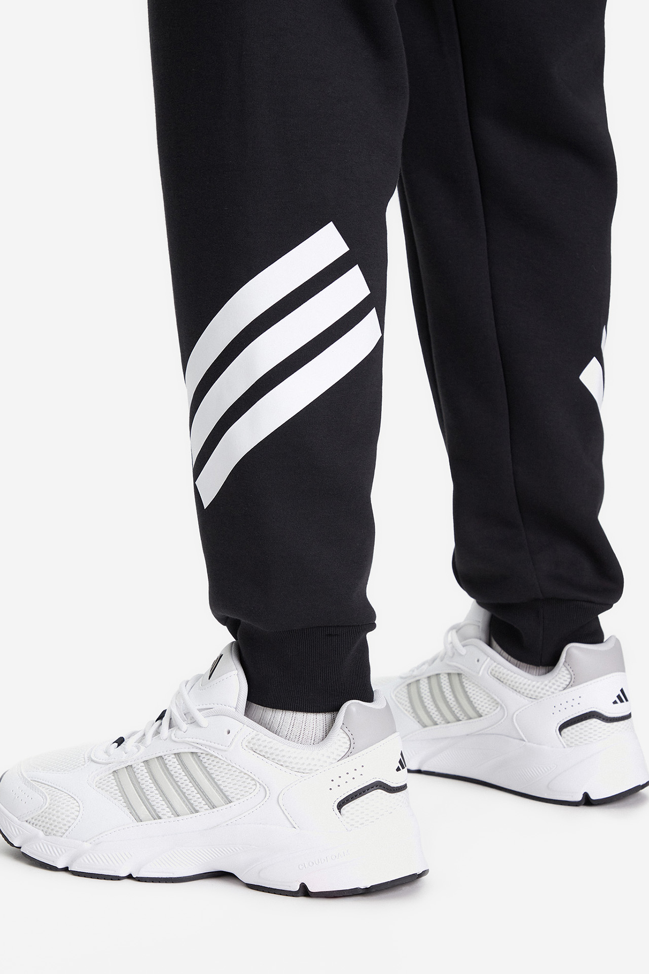 Dół nogawek spodni dresowych na modelu, widoczne buty.