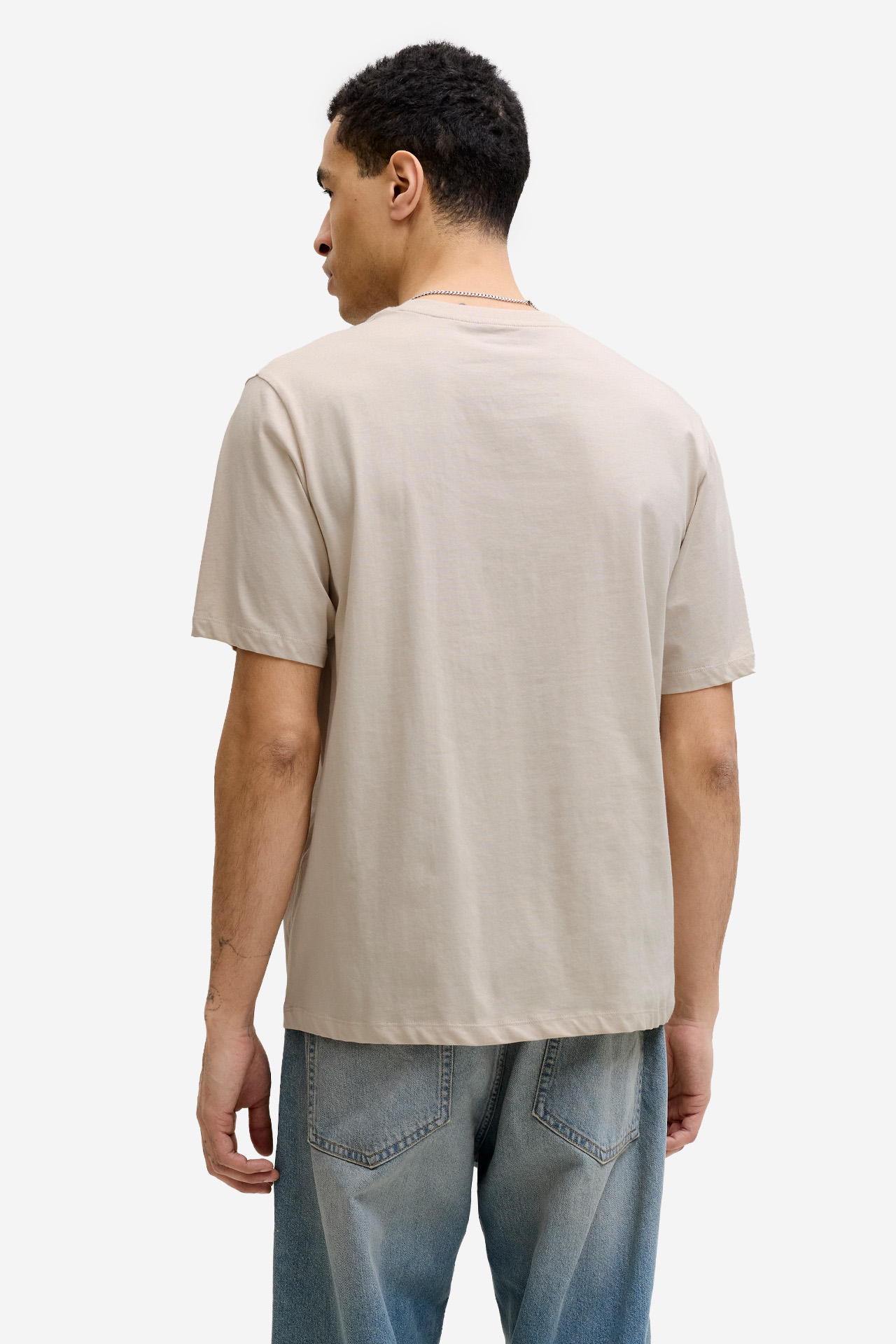 Model w T-shircie, widok od tyłu, ręce opuszczone w dół.